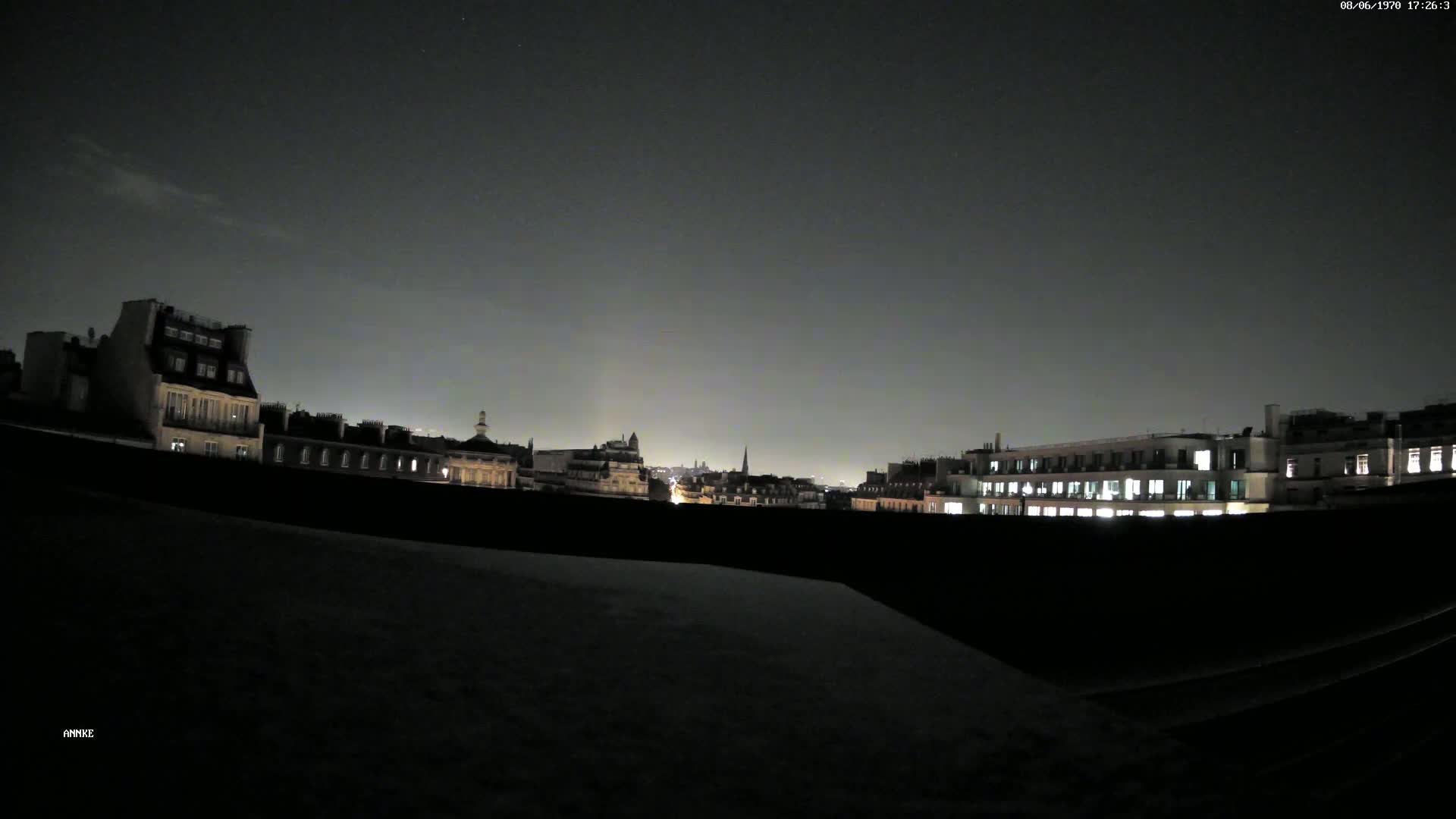 A nighttime cityscape of buildings with illuminated windows under a dark, mostly clear sky.