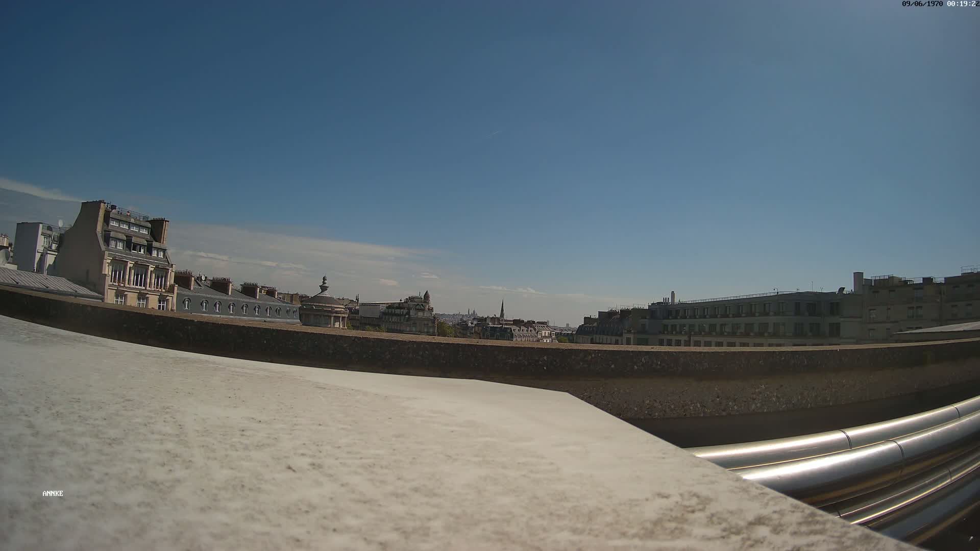 A rooftop view of a city on a clear, sunny day shows a row of buildings with metal pipes in the foreground.