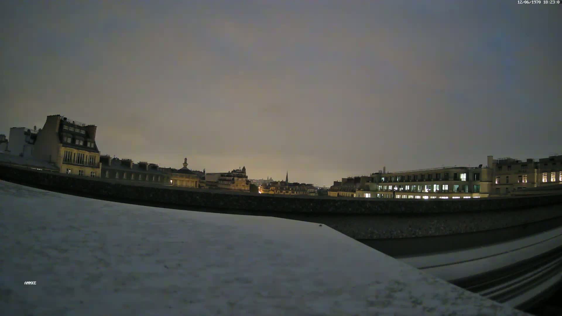 A snow-covered rooftop overlooks a city skyline at night under a dusky sky.