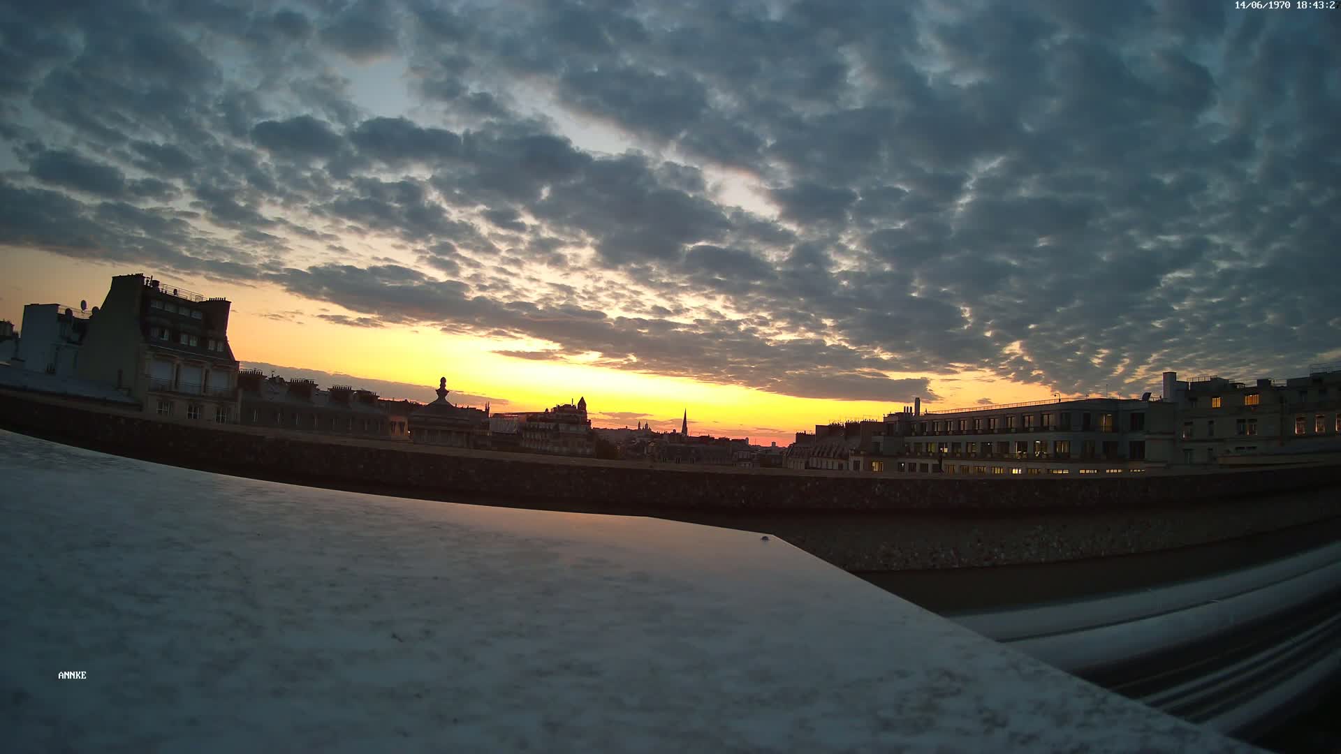 A city skyline at sunset under a cloudy sky, viewed from a high vantage point.