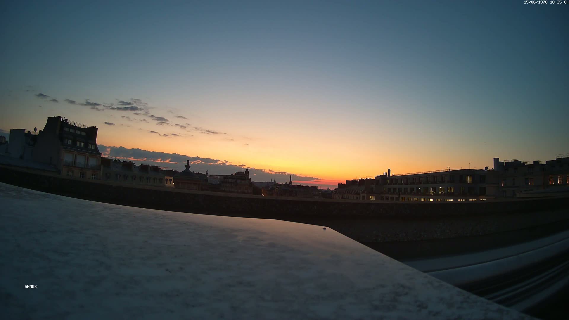 A city skyline at sunset, with the orange and yellow hues of the setting sun reflecting on a flat surface in the foreground.