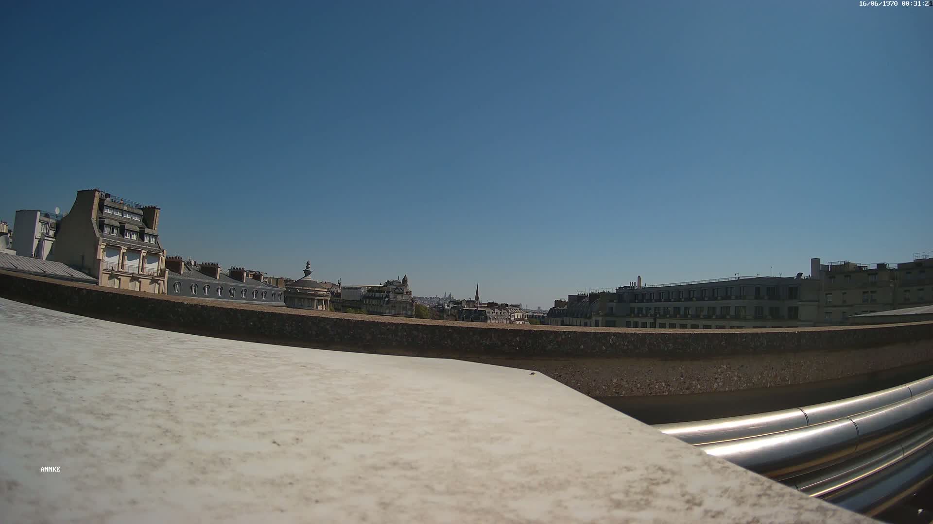 A rooftop view on a clear, sunny day shows a cityscape of buildings with gray slate roofs.