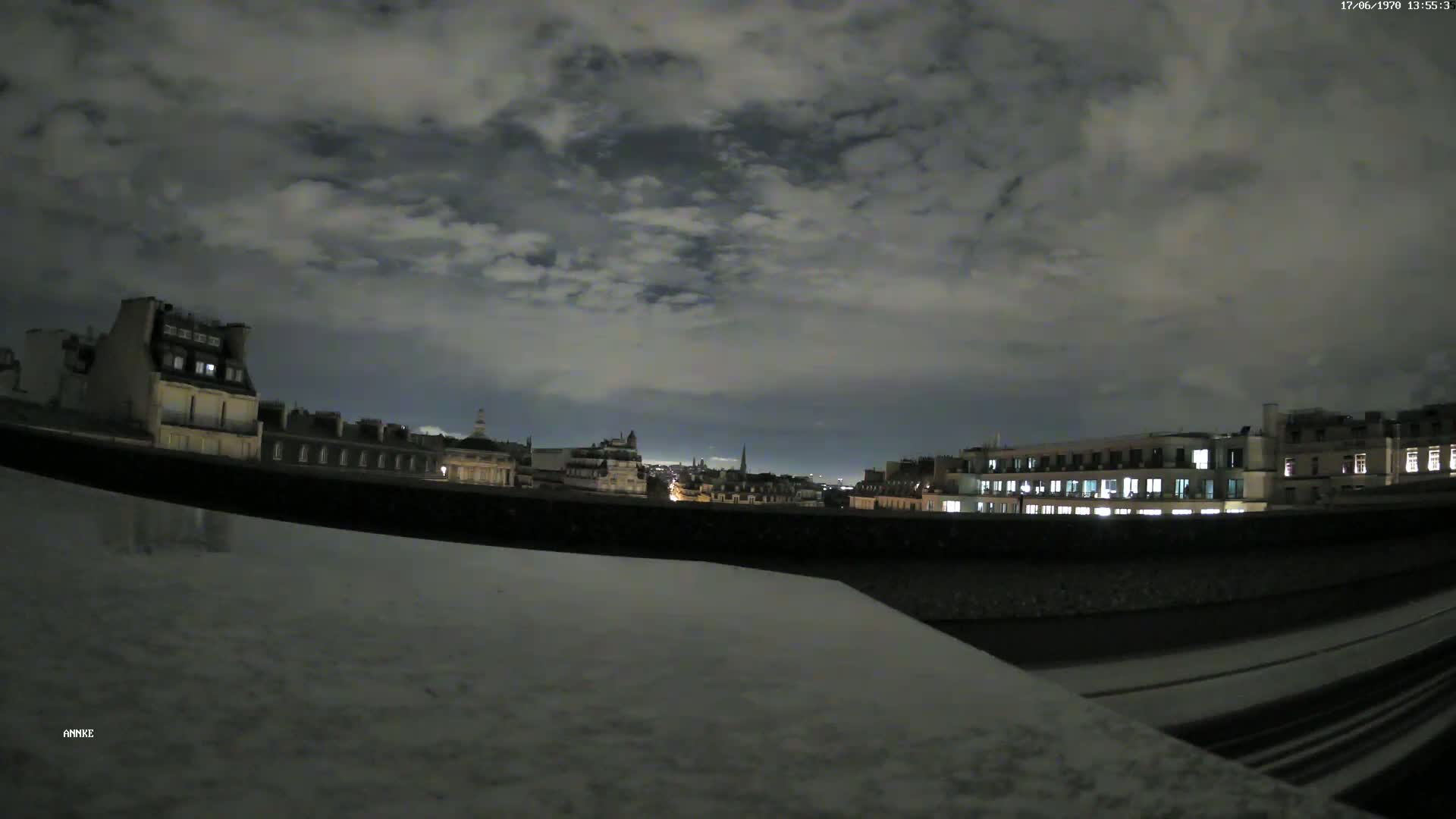 A nighttime cityscape view from a rooftop shows a partly cloudy sky over illuminated buildings.