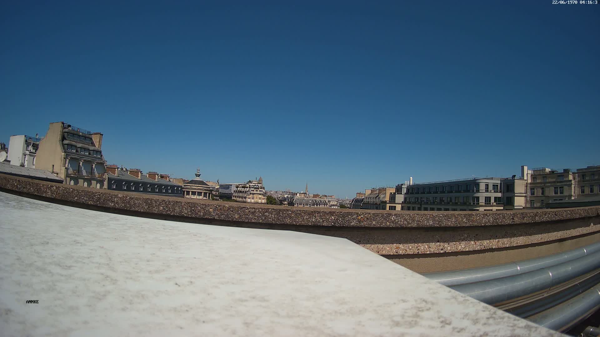 A cityscape of European-style buildings is visible from a rooftop under a clear blue sky.