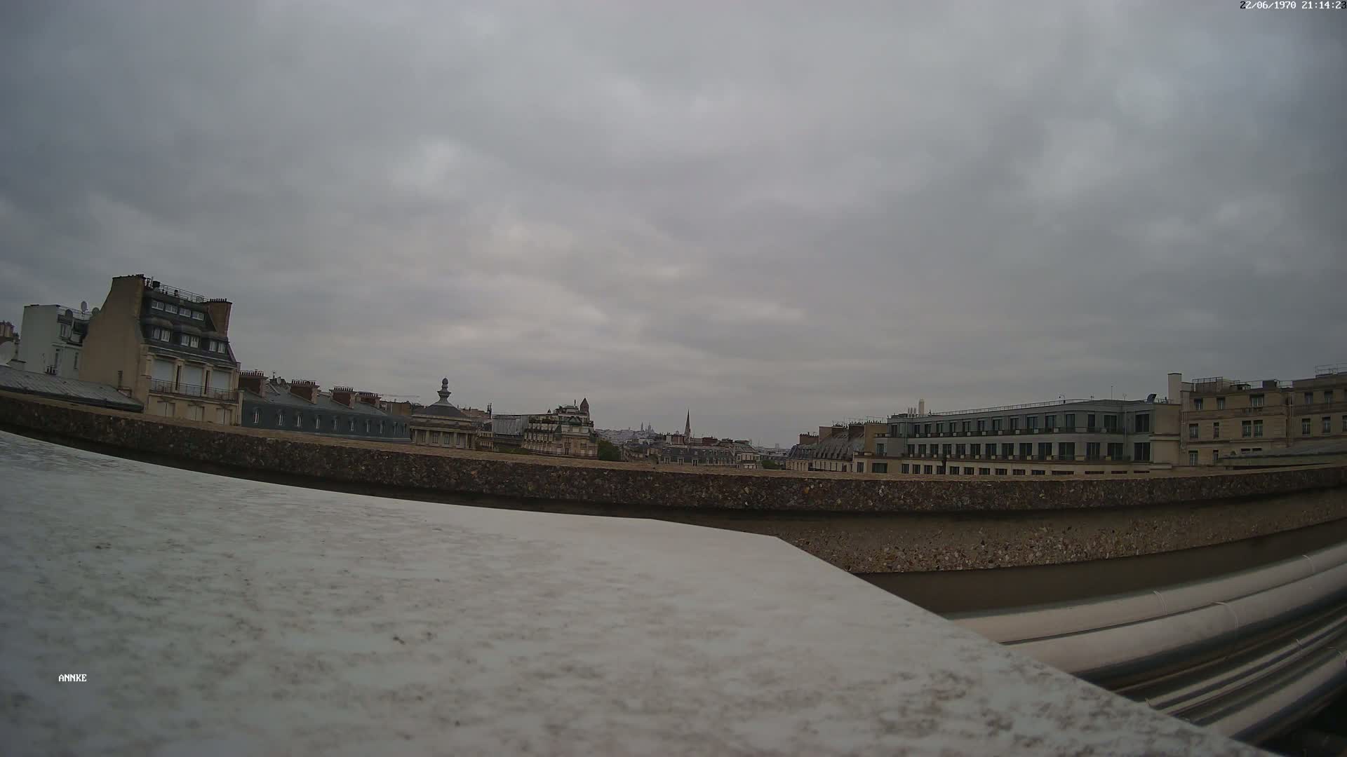 A cityscape of multi-story buildings is visible under an overcast sky.