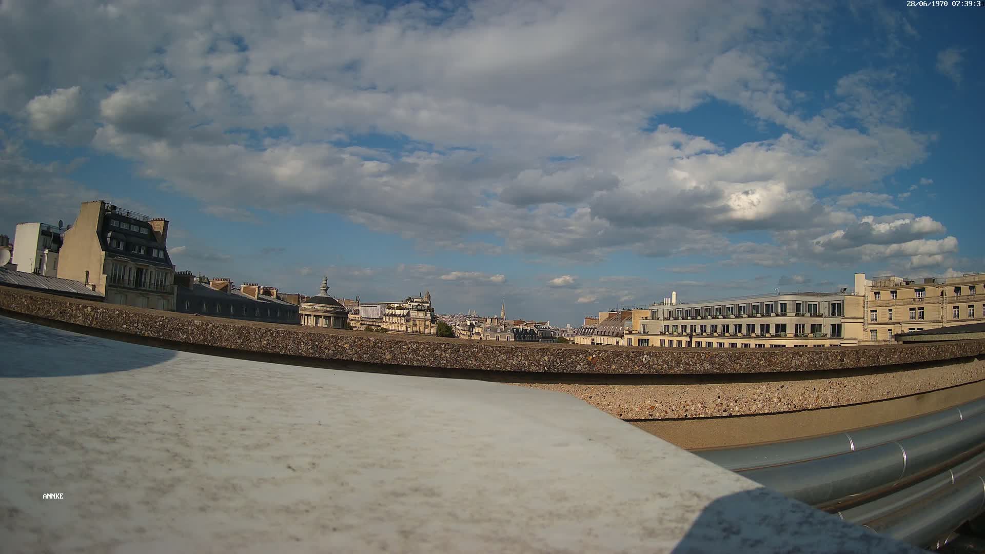 A partly cloudy sky overlooks a cityscape of European-style buildings from a rooftop vantage point.