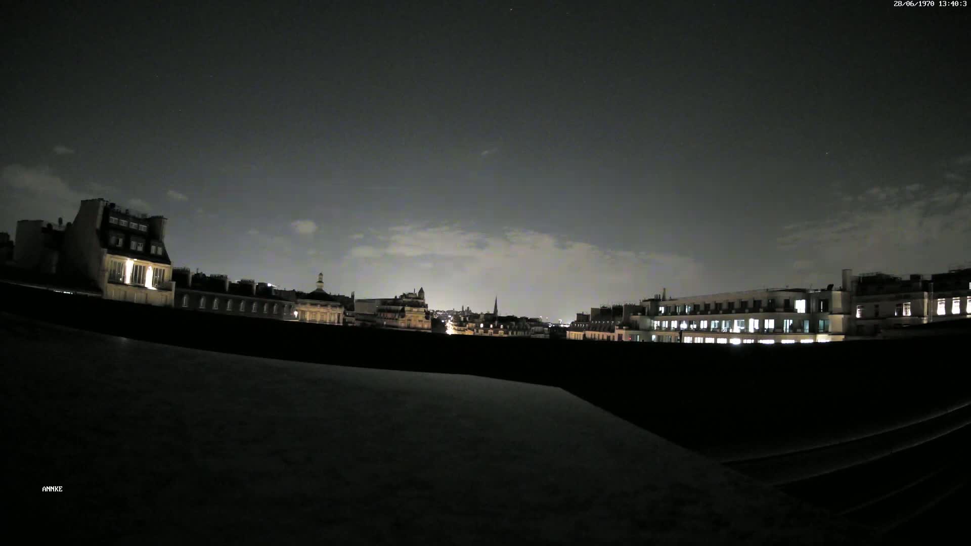 A nighttime cityscape of buildings with illuminated windows under a mostly cloudy sky.