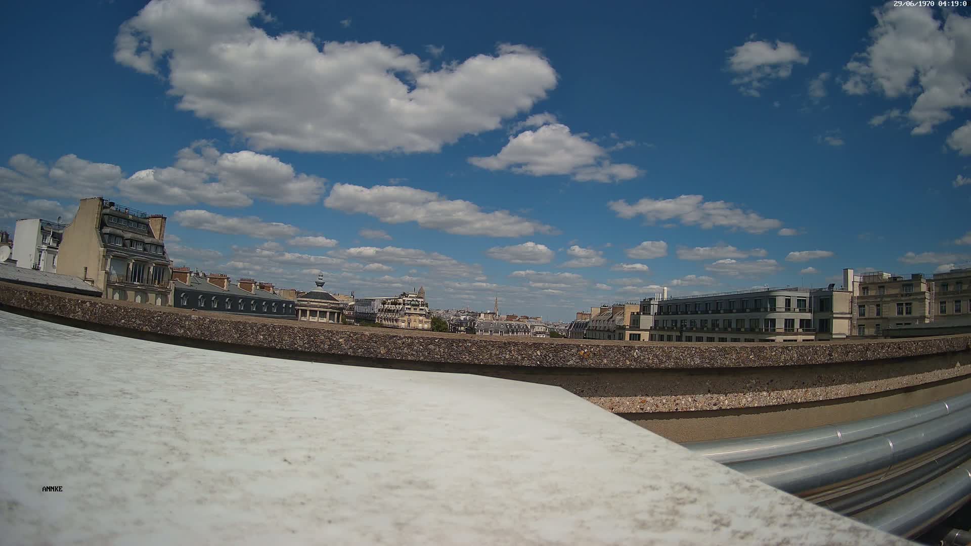 A rooftop view of Parisian buildings under a partly cloudy, sunny sky.