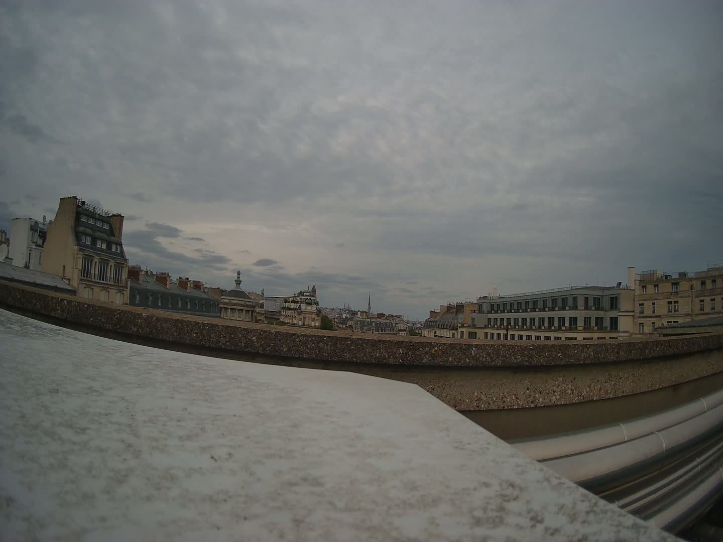 A city skyline of multi-story buildings under a cloudy sky is viewed from a rooftop.