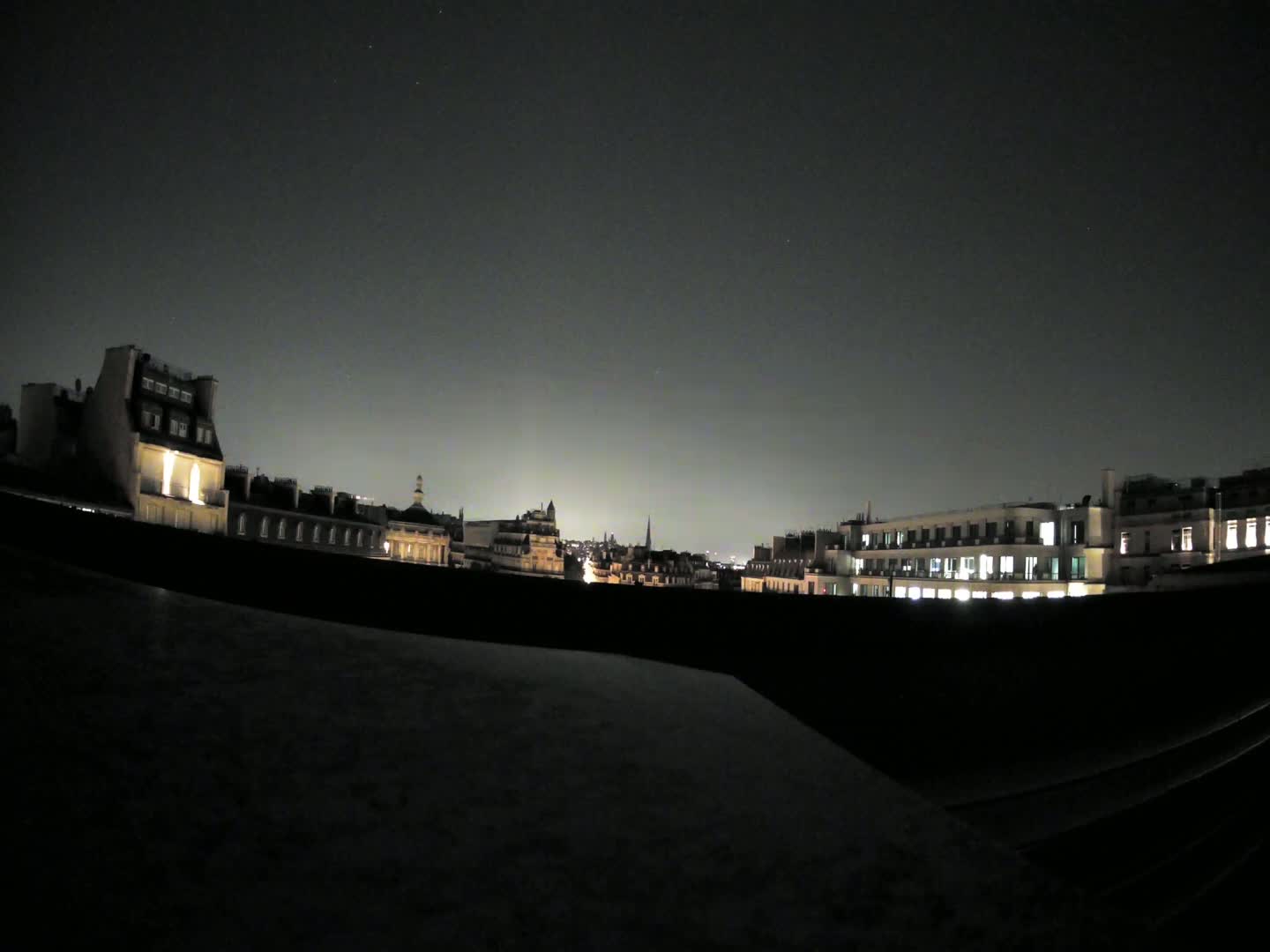 A nighttime cityscape of buildings with illuminated windows under a dark, clear sky.