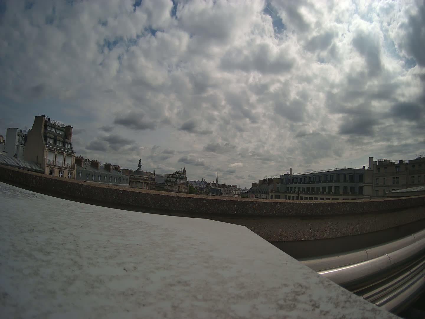 A partly cloudy sky overlooks a city skyline of Parisian-style buildings from a rooftop vantage point.