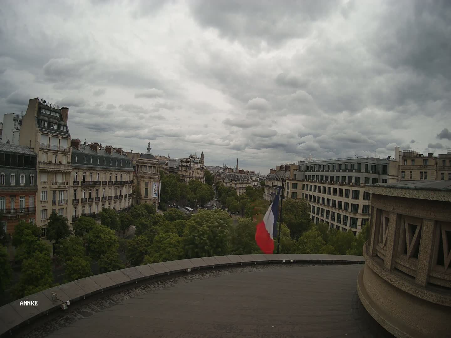 A city view of Parisian buildings under a cloudy sky, with a French flag waving in the foreground.