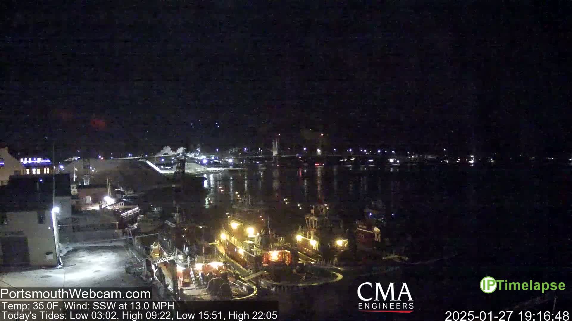 A nighttime harbor scene shows several docked tugboats illuminated by lights, under a clear, dark sky.