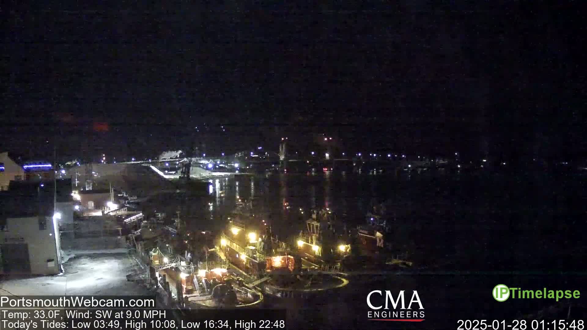 A nighttime harbor scene shows several lit-up tugboats moored near a dark shoreline under a clear, dark sky.