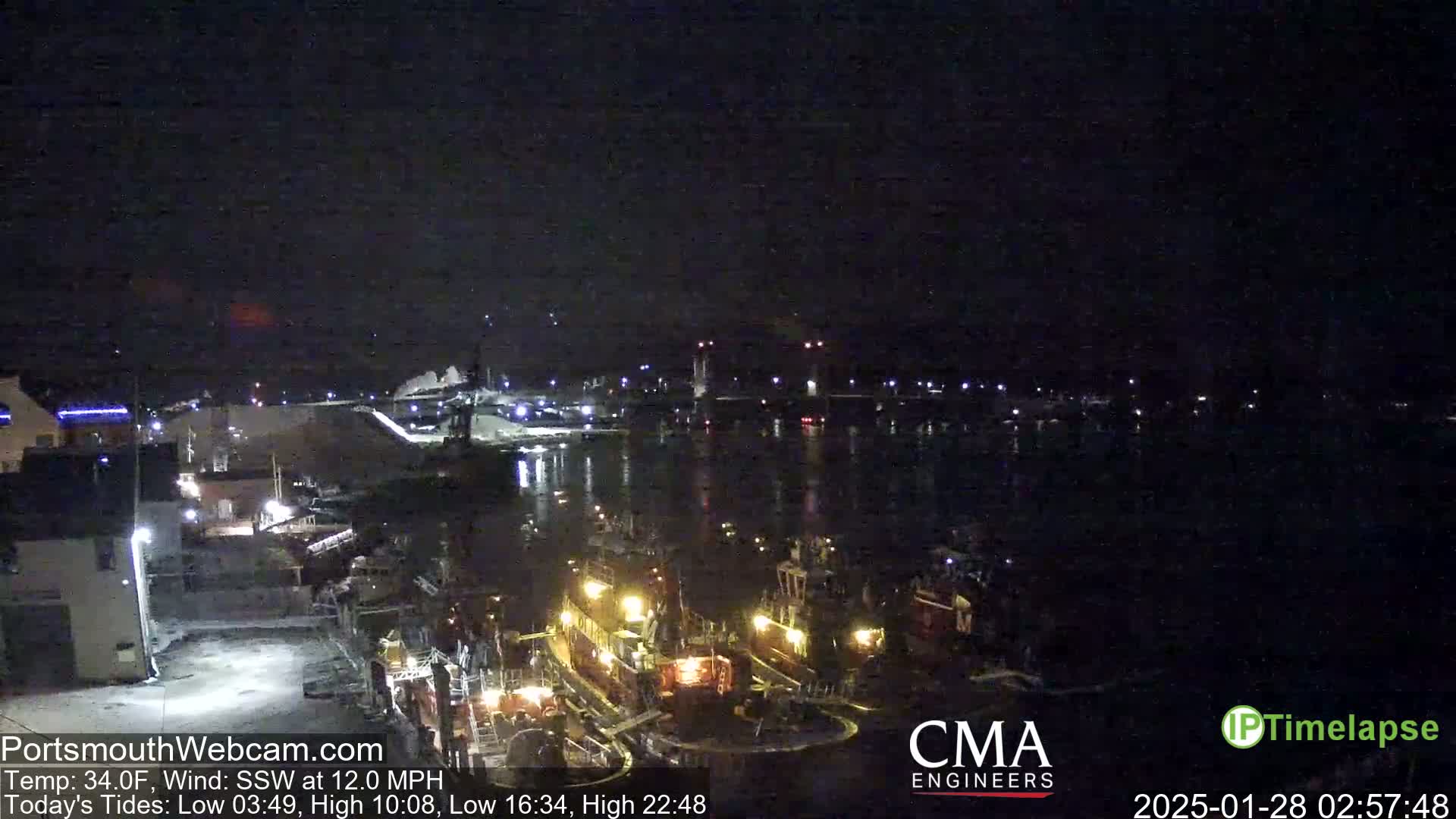 A nighttime harbor scene shows several docked tugboats illuminated by their lights under a dark, clear sky.