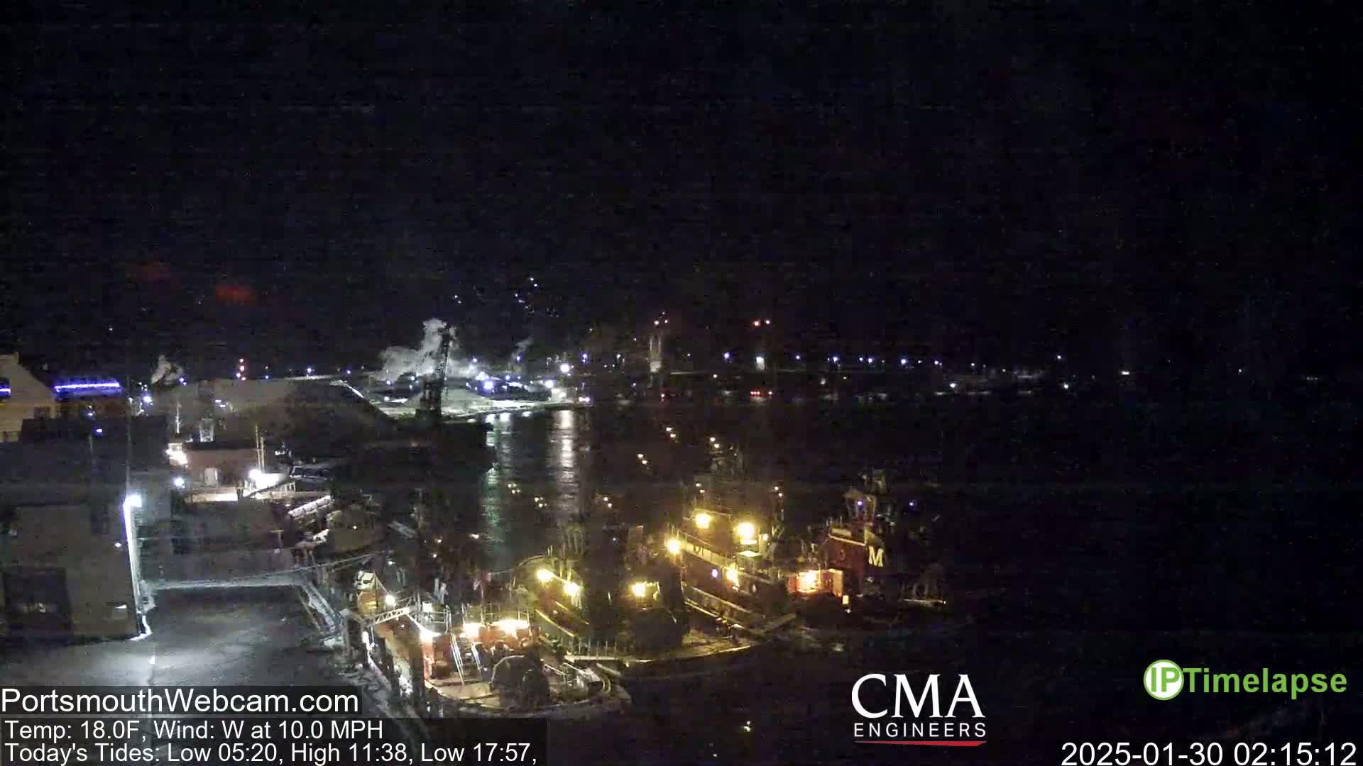 A nighttime harbor scene shows several illuminated tugboats moored near a waterfront, with calm water and a dark sky.