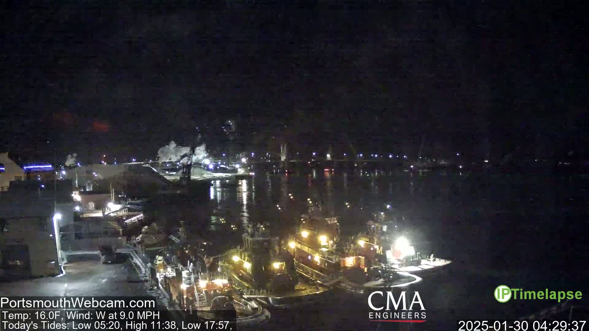 At night, several tugboats are moored near a dock under a dark, clear sky.