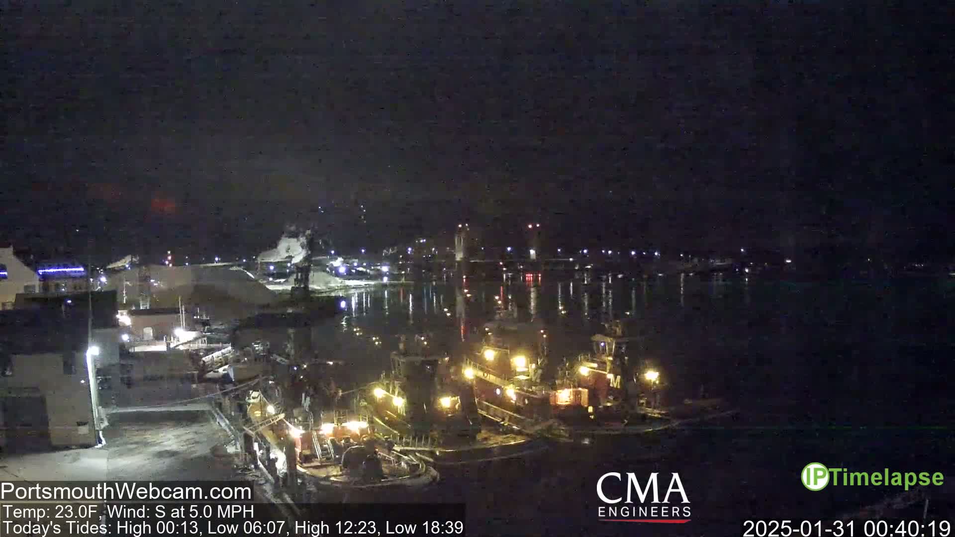 Several tugboats are docked at a waterfront at night under a dark sky.