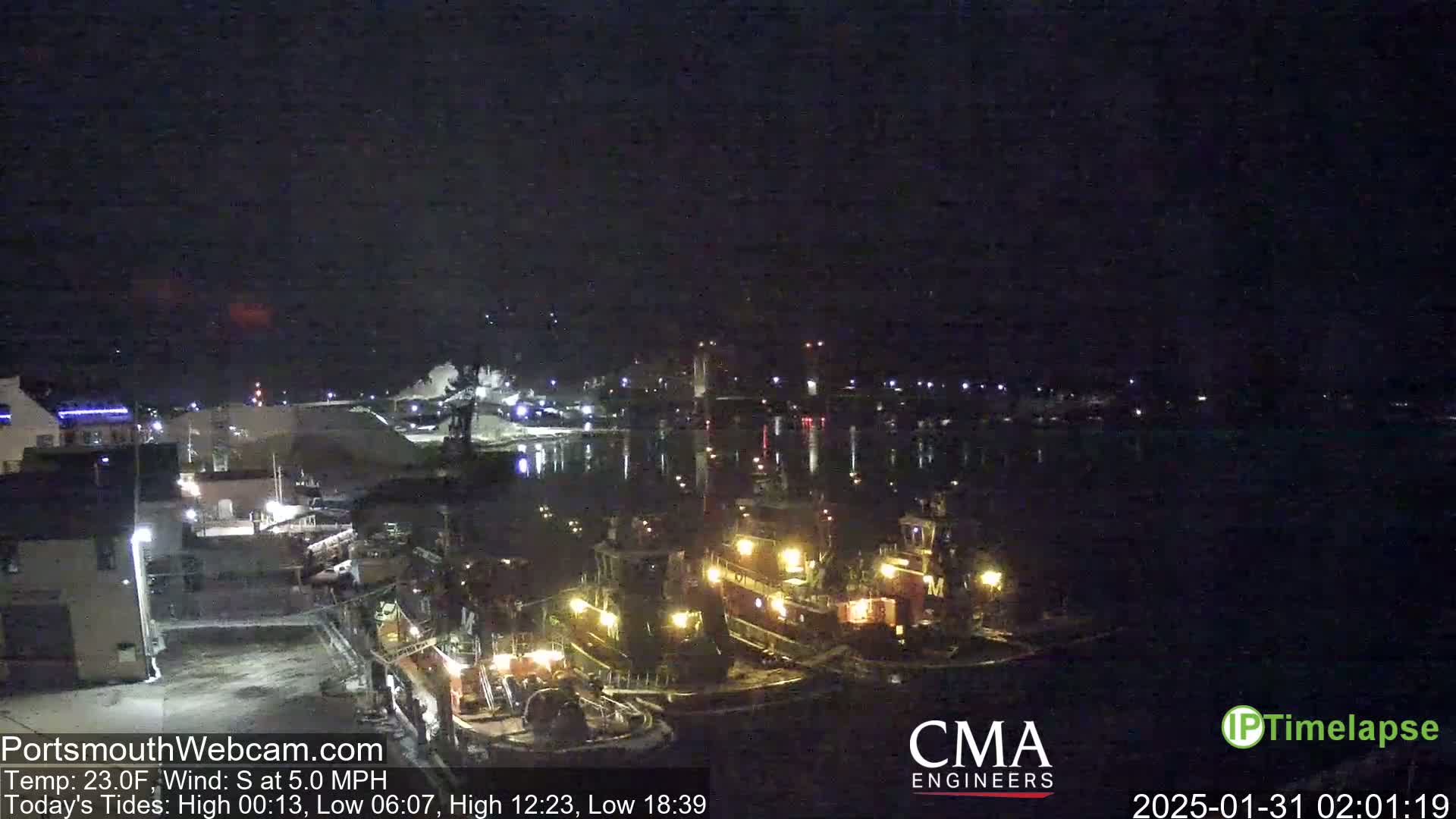 A nighttime view of a harbor with several tugboats docked, under a dark, clear sky.