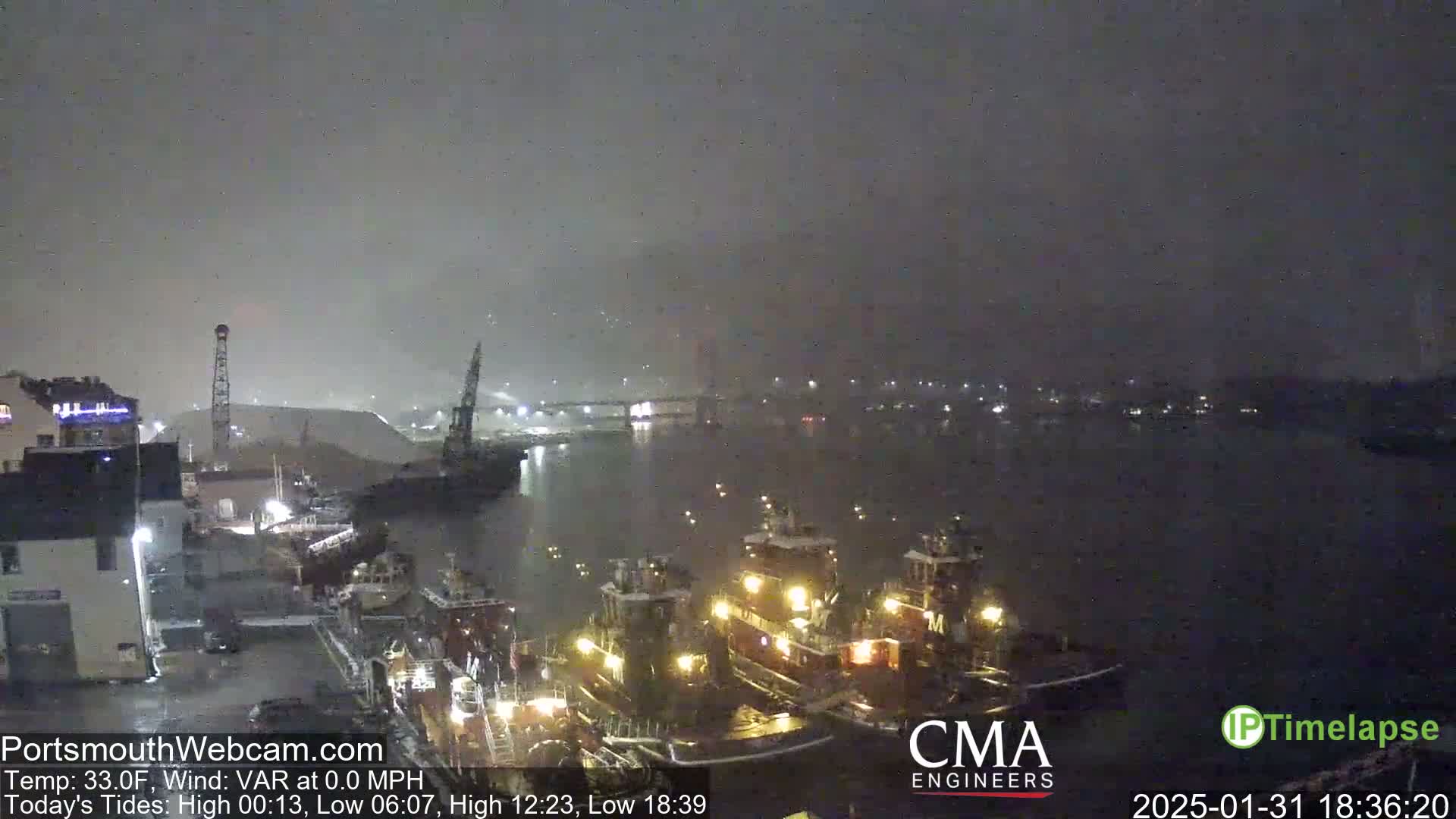 A nighttime view of a harbor with several docked tugboats under a hazy, dark sky.
