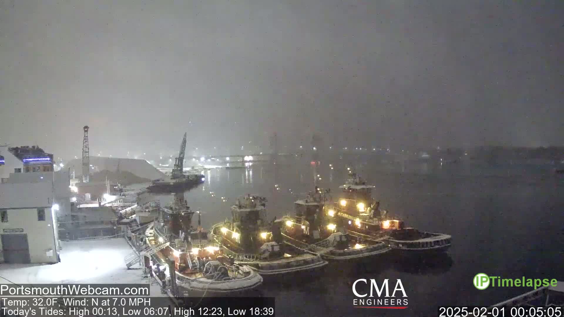 Several tugboats are docked at a snow-covered harbor during a nighttime snowstorm.