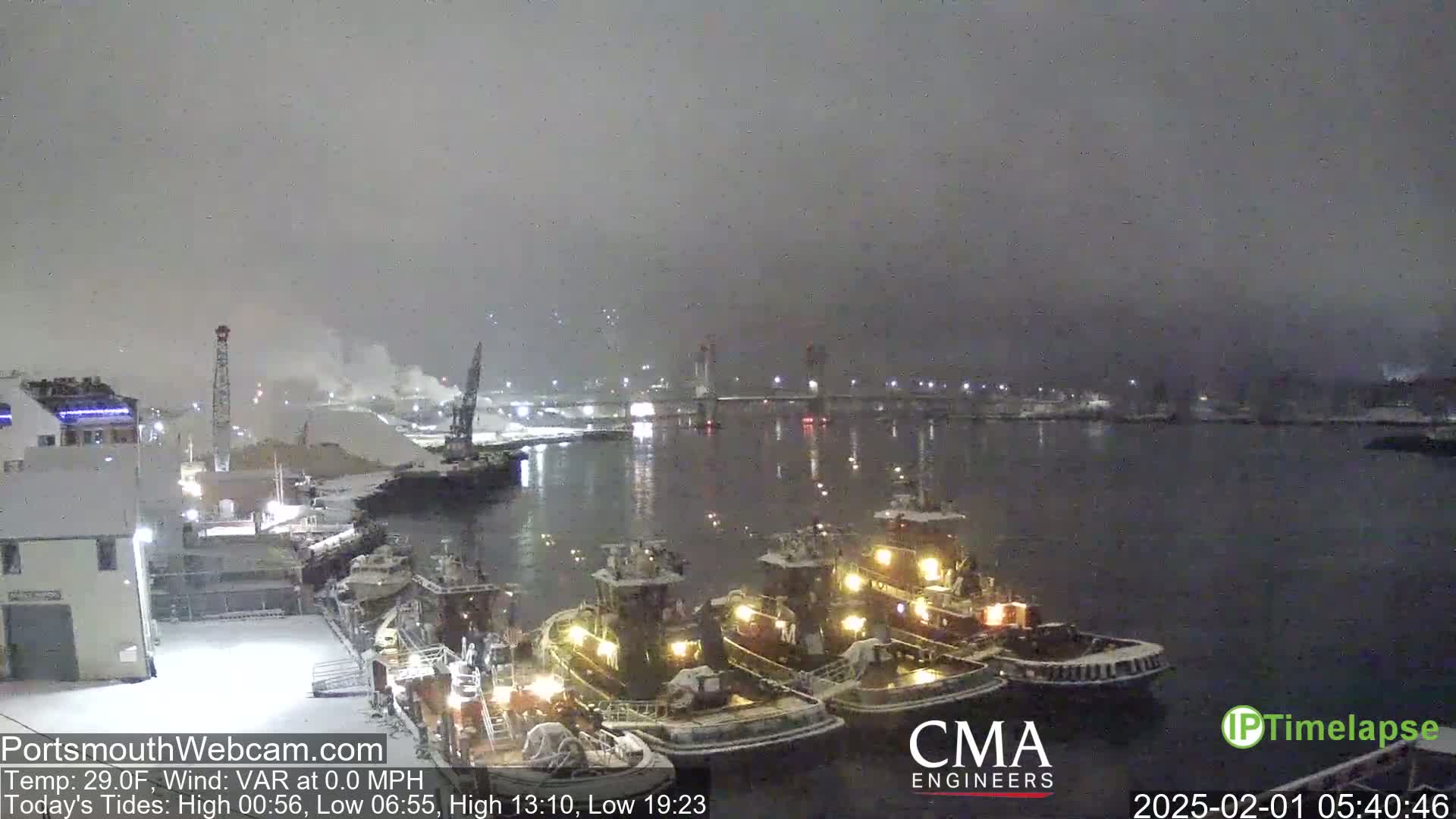 Three tugboats are docked at a snow-covered harbor under a dark, overcast sky.