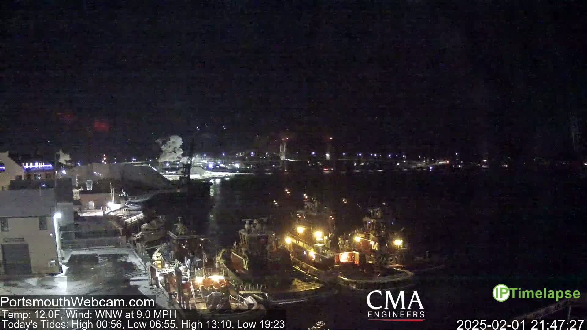 A nighttime view of a harbor with several tugboats moored alongside a dock, under a clear, dark sky.
