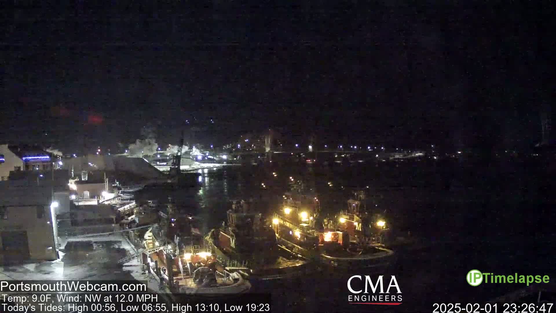 Several tugboats are moored at a dock at night in a harbor, under a dark, clear sky with a northwest wind.