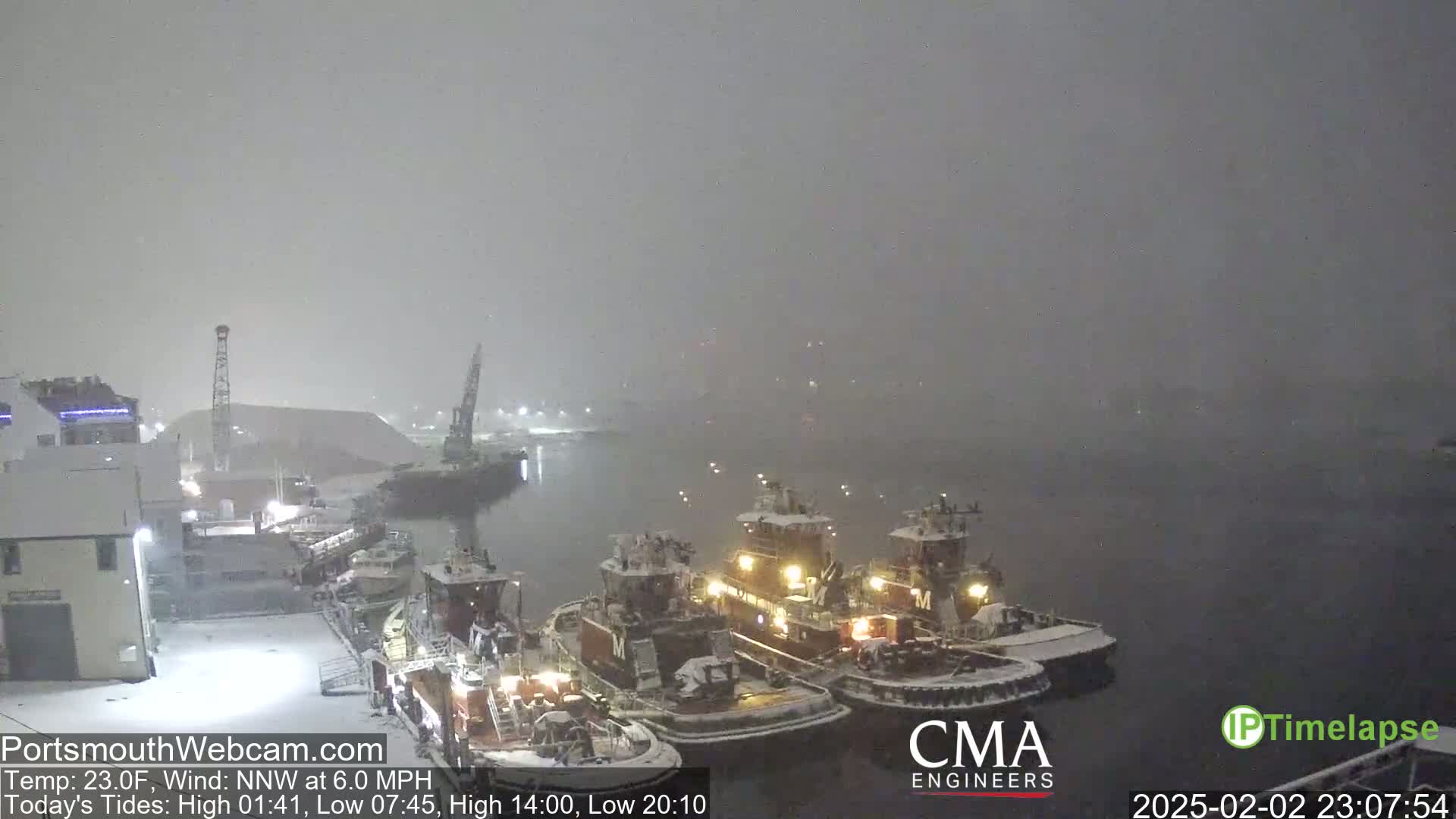 Several tugboats are docked in a harbor during a heavy snowfall.