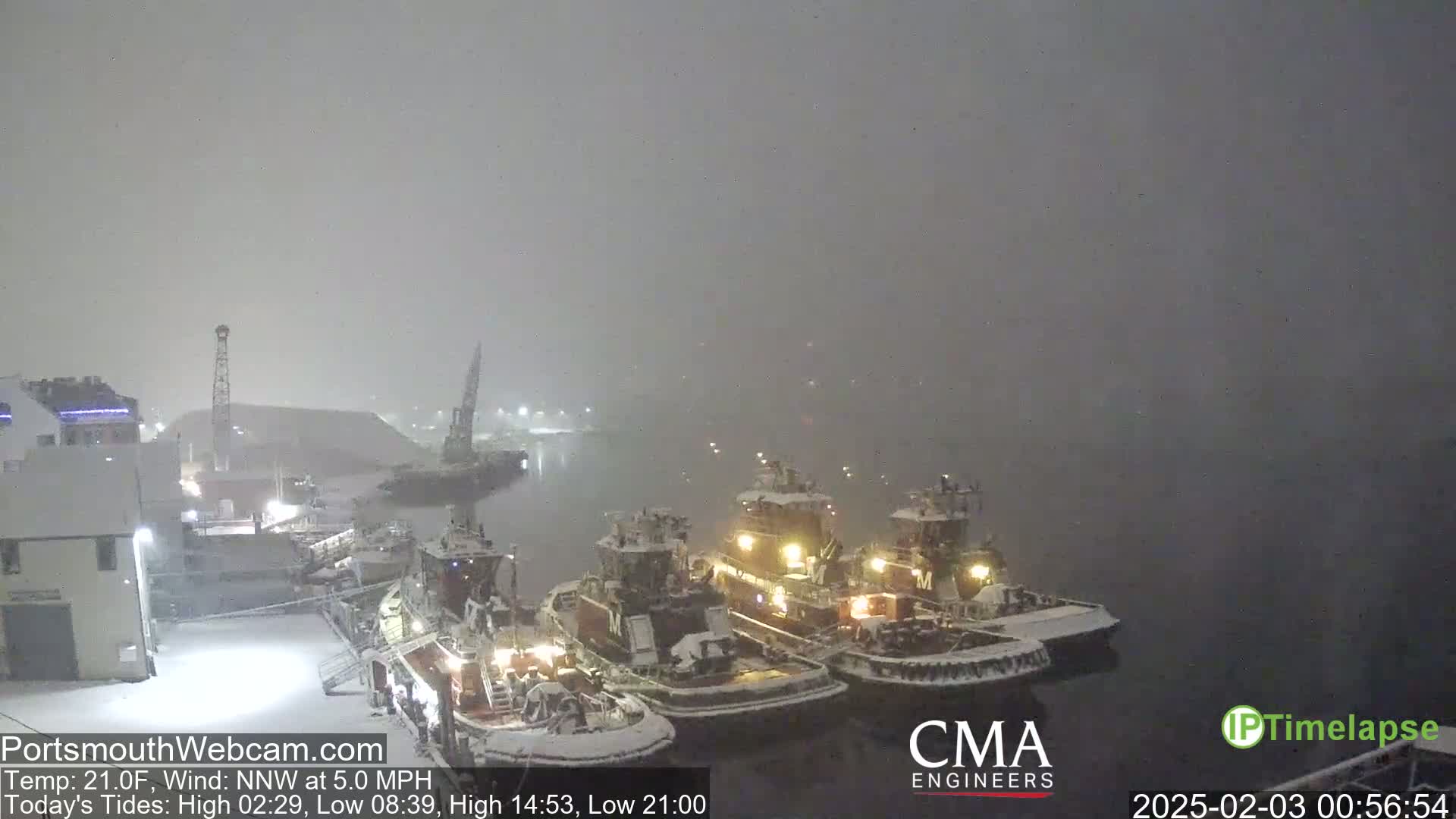 Three tugboats are docked in a snowy harbor at night.