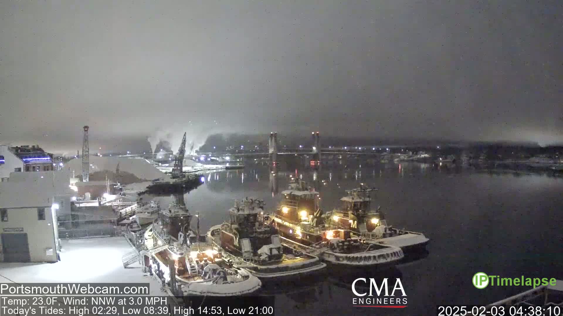 Three tugboats are docked at a snow-covered harbor at night under a dark, overcast sky.