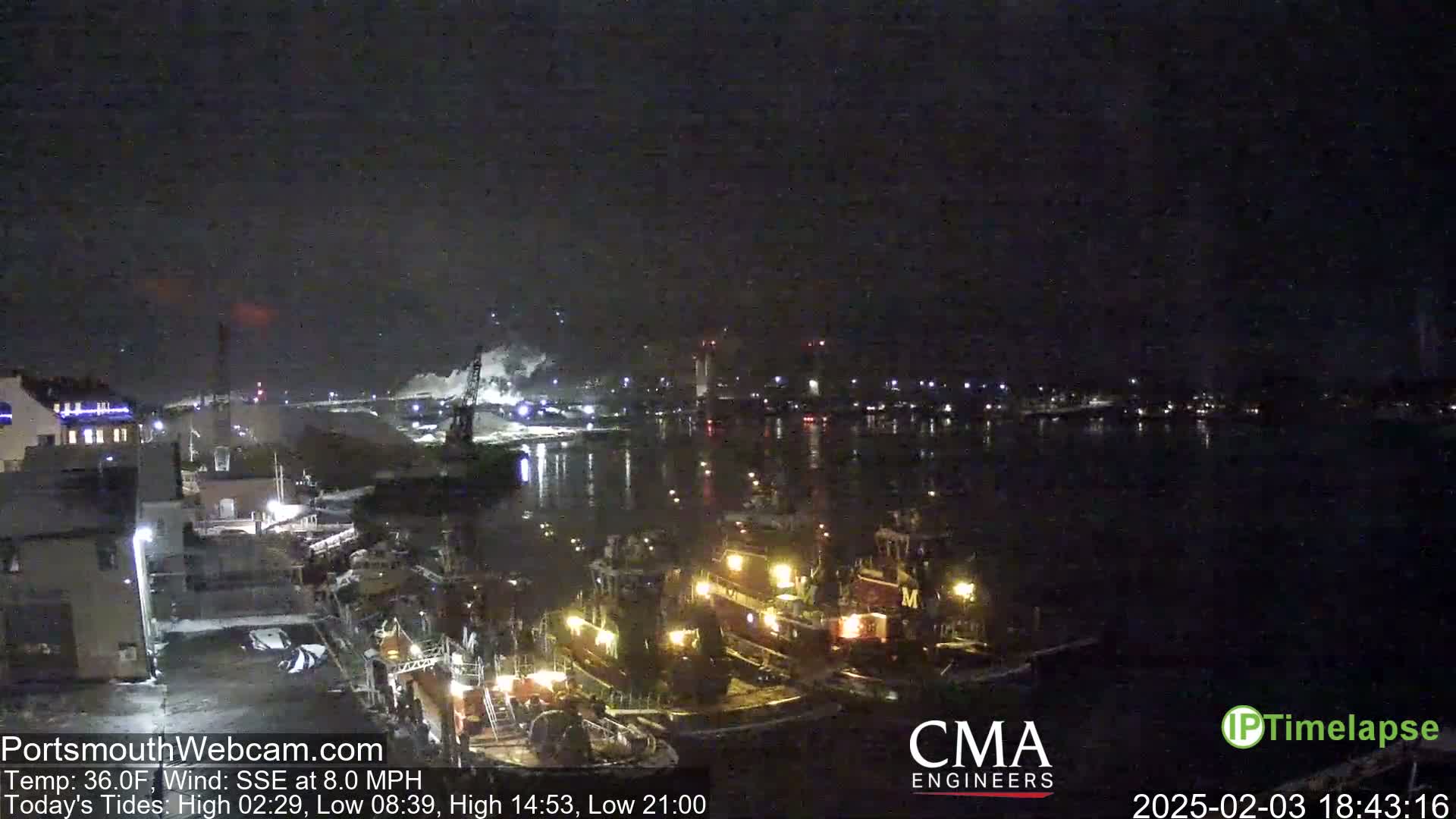 Several tugboats are moored at a dock at night under a dark sky.