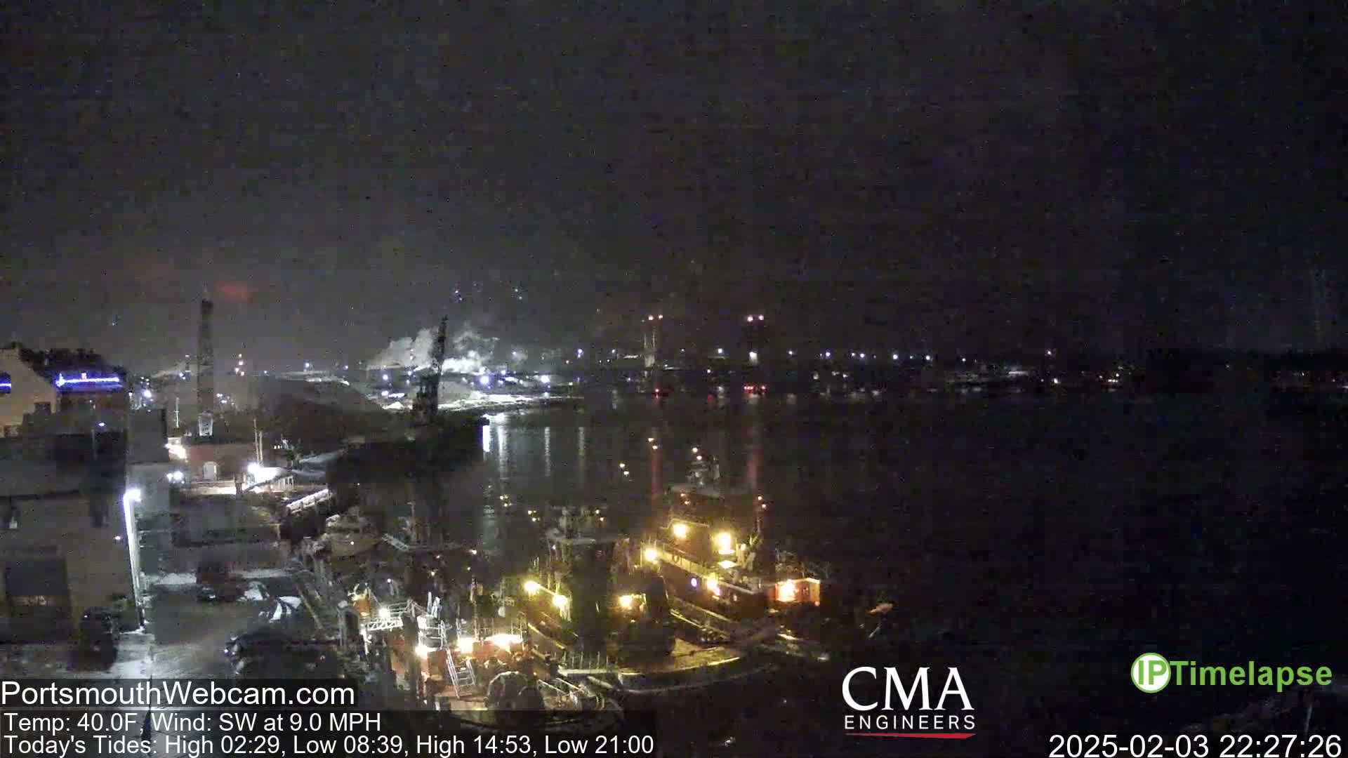A nighttime view of a harbor with several tugboats docked, under a dark sky with a southwest wind.
