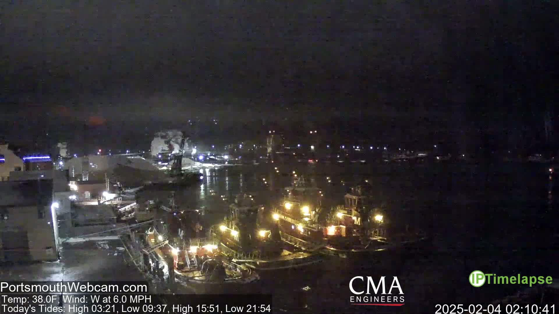 A nighttime view of a harbor with several tugboats docked, under a dark, cloudy sky.