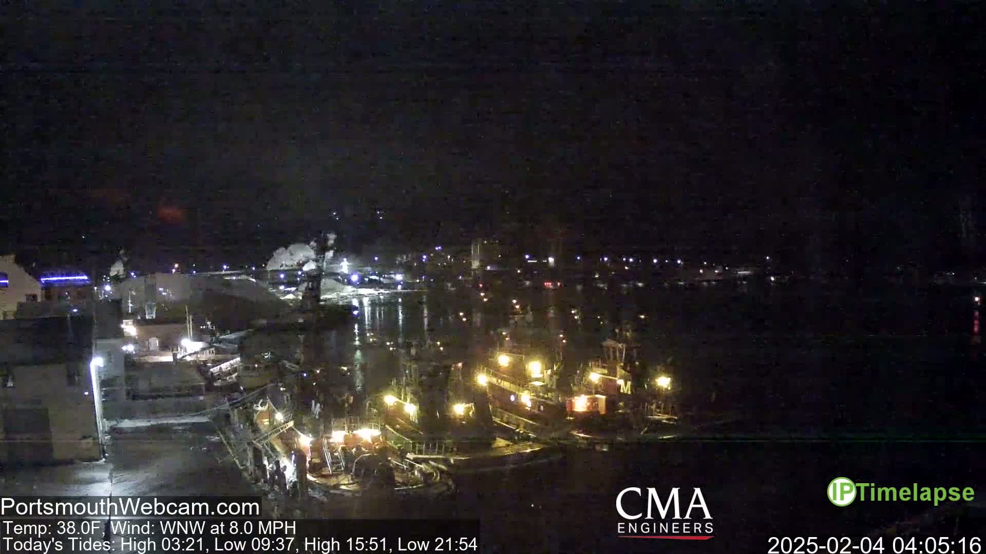 A nighttime view of a harbor with several docked boats illuminated by their lights, under a clear, dark sky.