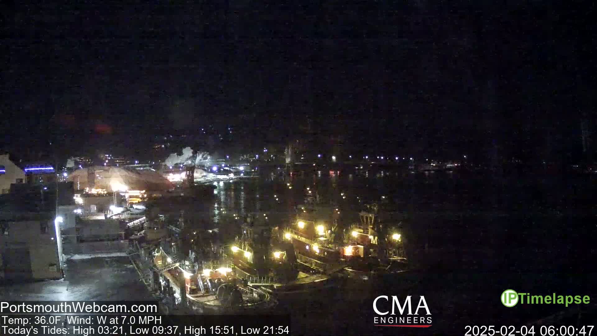At night, several tugboats are docked at a harbor, with a large pile of material visible in the background under a clear, dark sky.