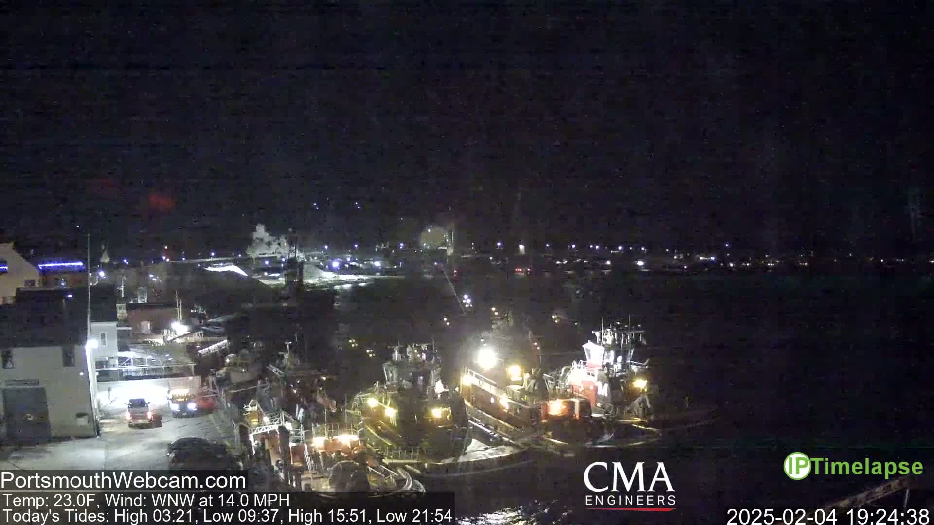 A nighttime harbor scene shows several tugboats moored alongside a dock under a clear, dark sky.