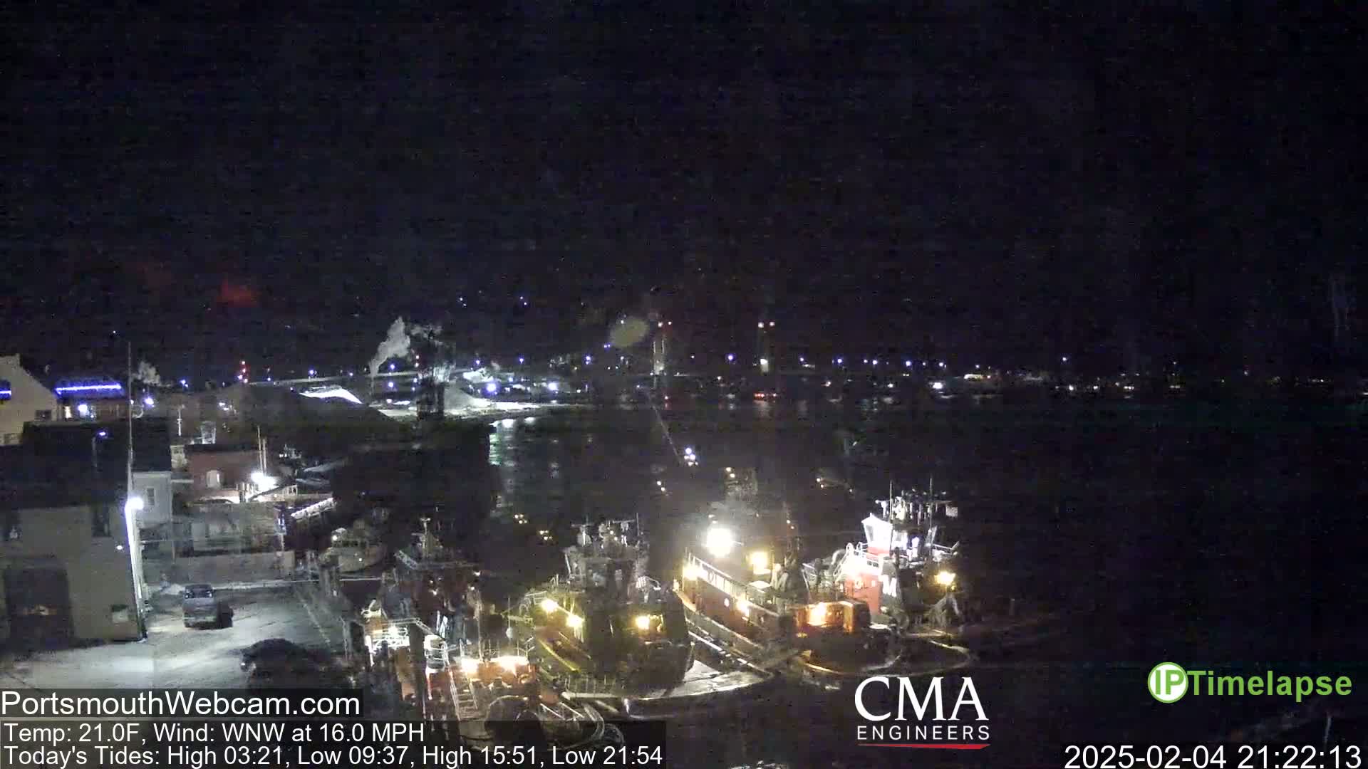 At night, under a dark sky with a wind of 16 mph from the west-northwest, several boats are docked at a harbor, with lights illuminating the scene.