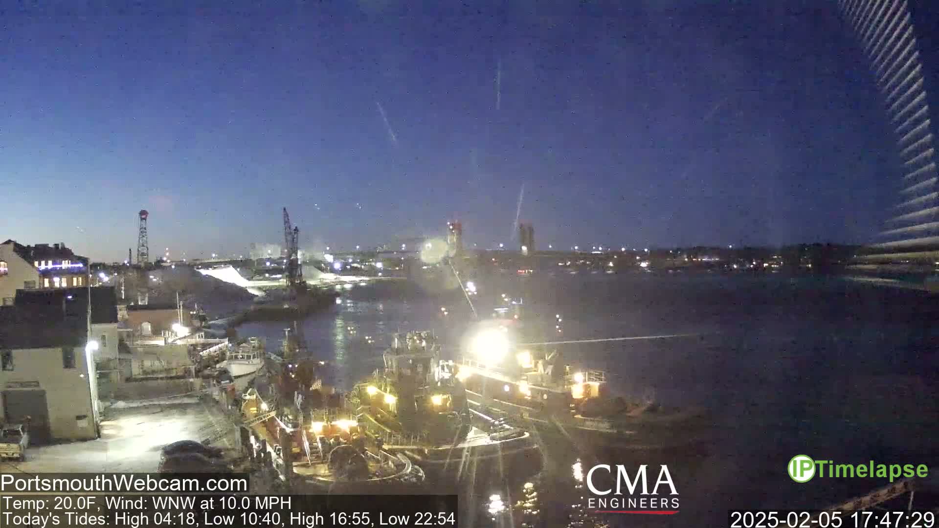 Several tugboats are docked at a waterfront harbor at night under a dark blue, clear sky with a light wind.