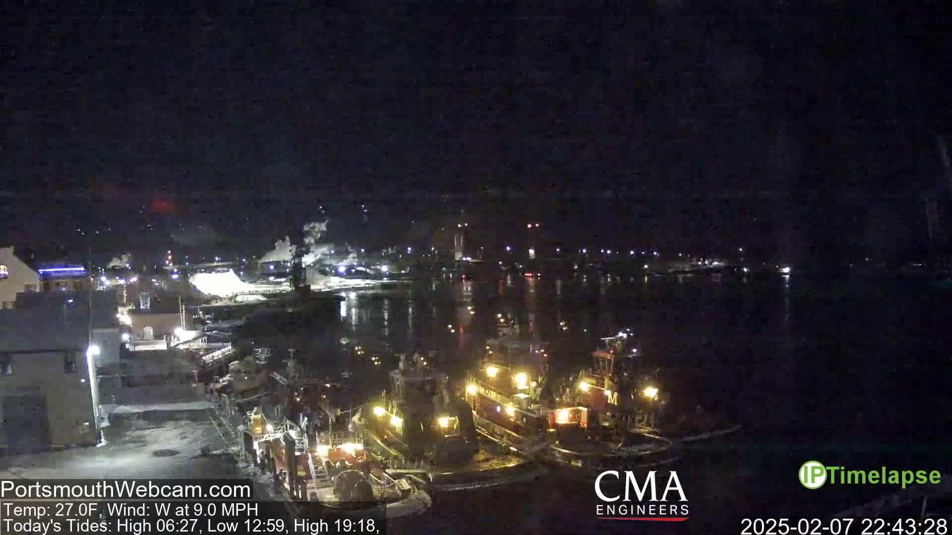 A nighttime harbor scene shows several tugboats moored at a dock under a dark, clear sky.