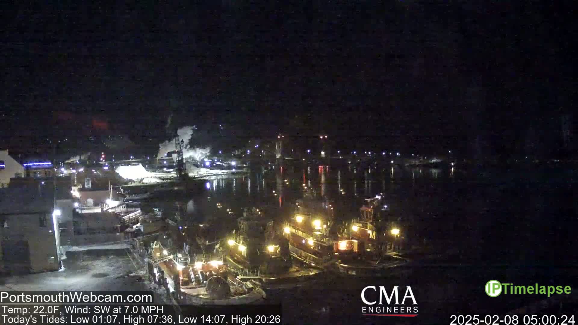 A nighttime view of a harbor with several illuminated tugboats docked, under a dark sky with a southwest wind.