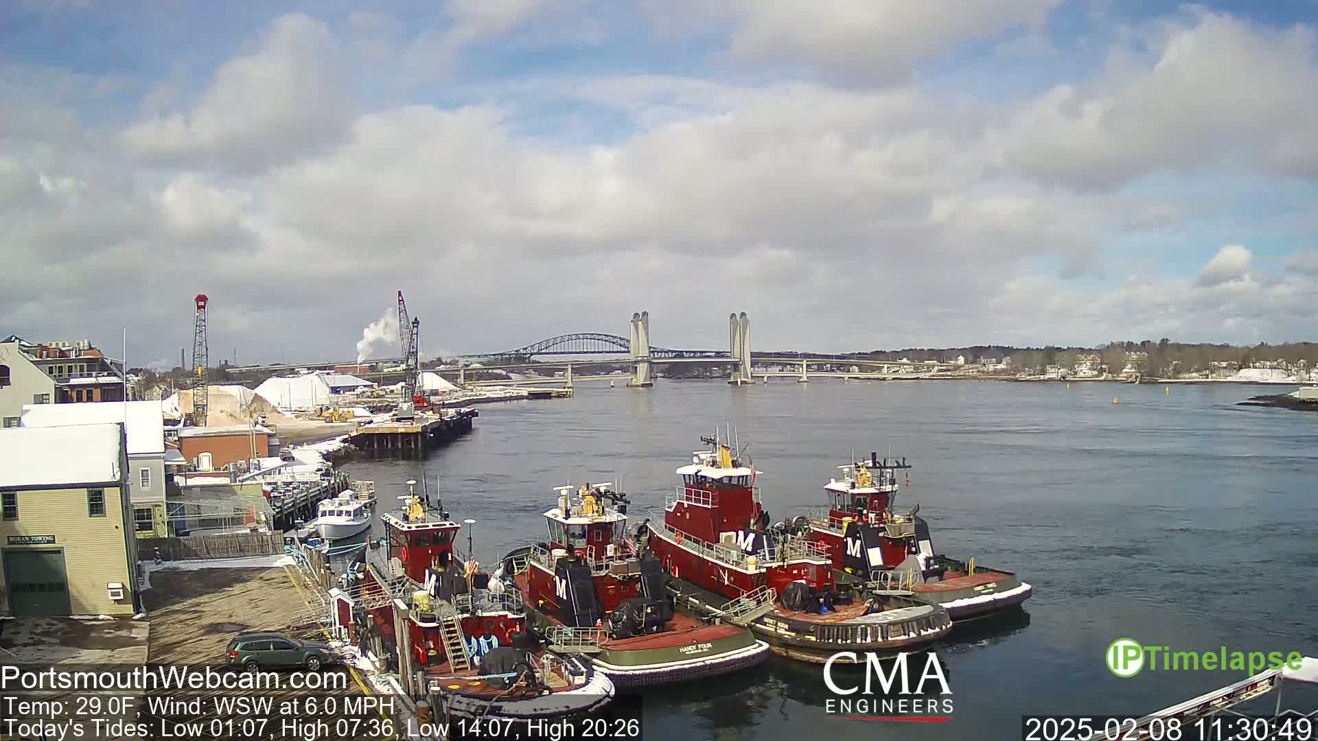 Several tugboats are moored at a dock near a bridge on a partly cloudy day with a temperature of 29°F and a wind from the west-southwest at 6.0 mph.