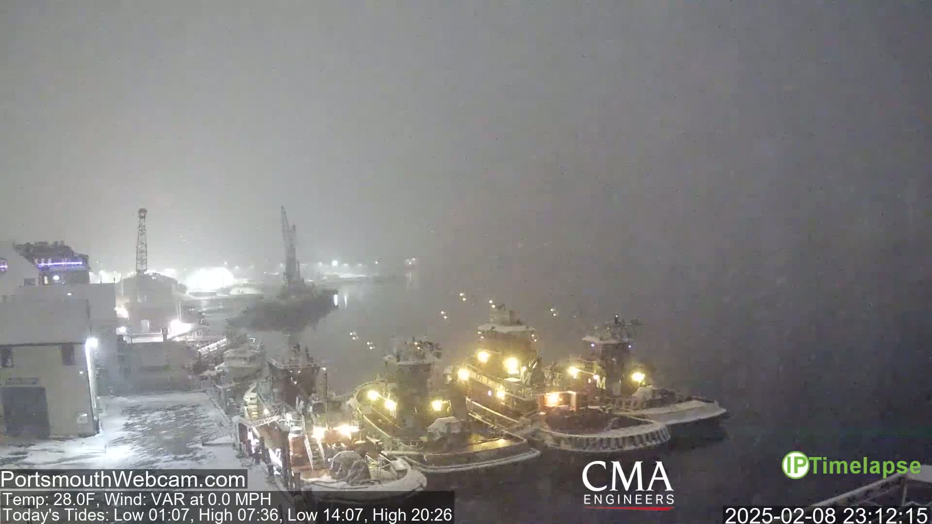 Three tugboats are moored at a dock in heavy snowfall.