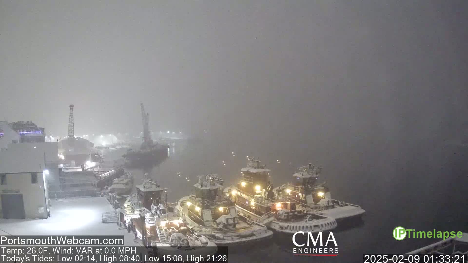 Several snow-covered tugboats are docked in a harbor during a heavy snowfall.