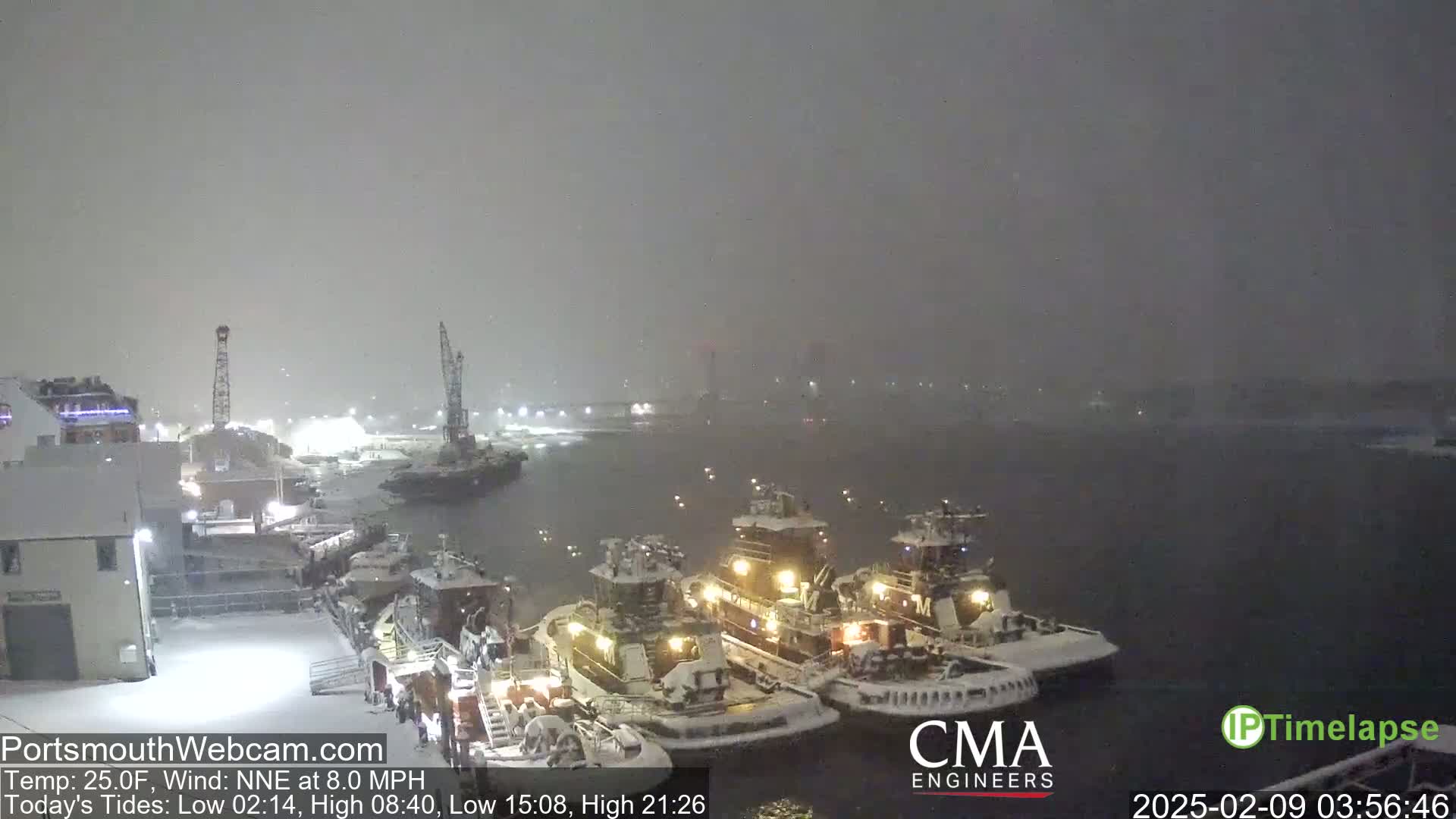 Three tugboats are docked in a snow-covered harbor during a heavy snowfall with a NNE wind.