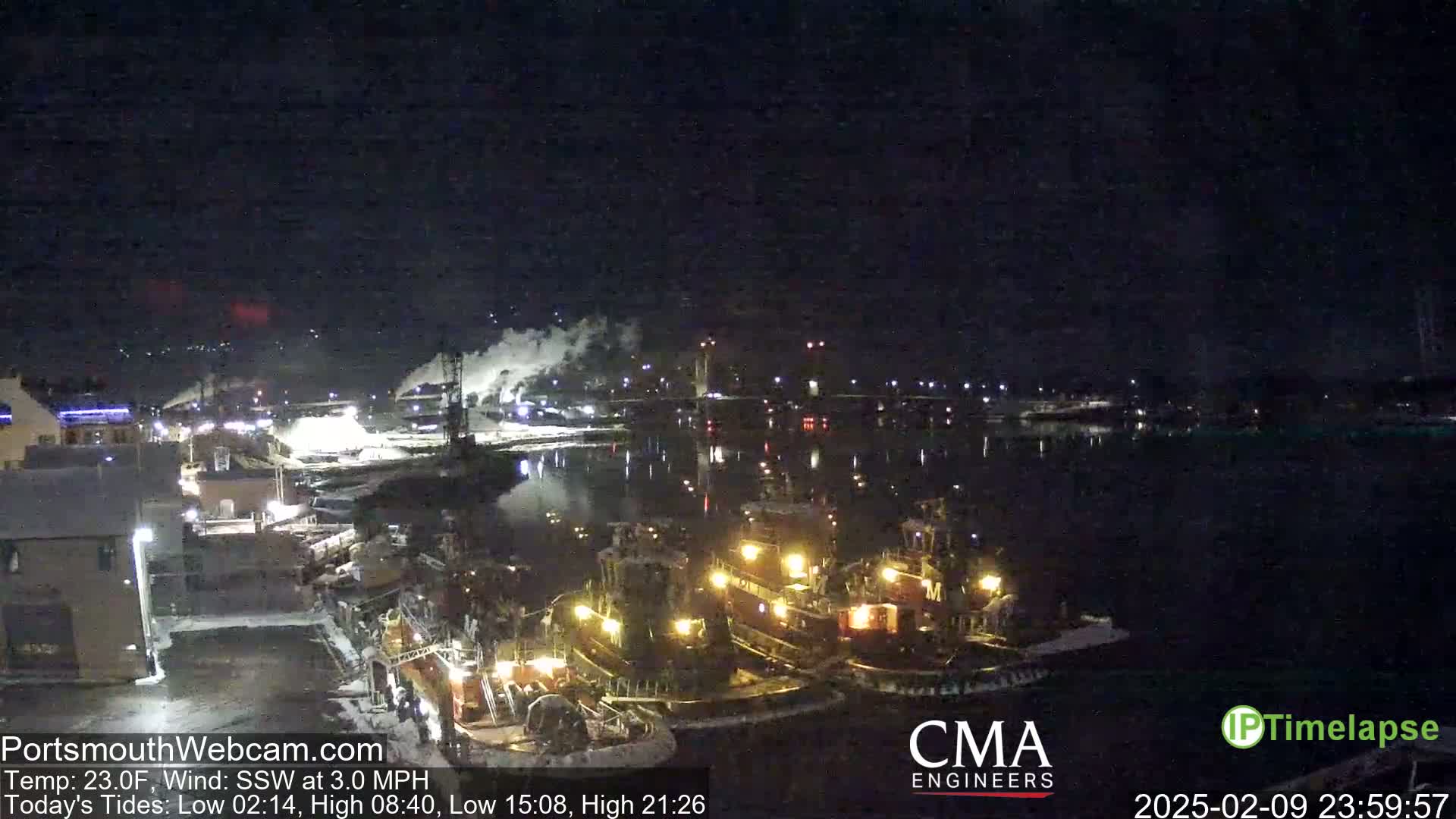 At night, several tugboats are moored at a dock next to a calm body of water under a dark sky.