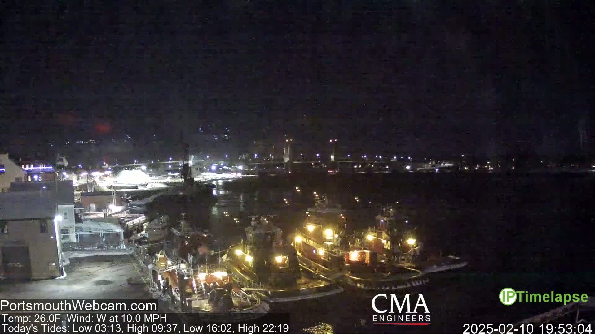Several tugboats are moored at a dock at night under a clear, dark sky with a west wind.