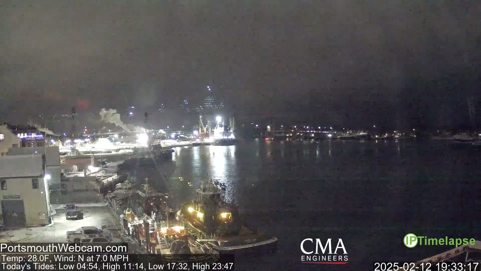 A nighttime harbor scene shows several ships and tugboats in calm water under a dark, hazy sky.