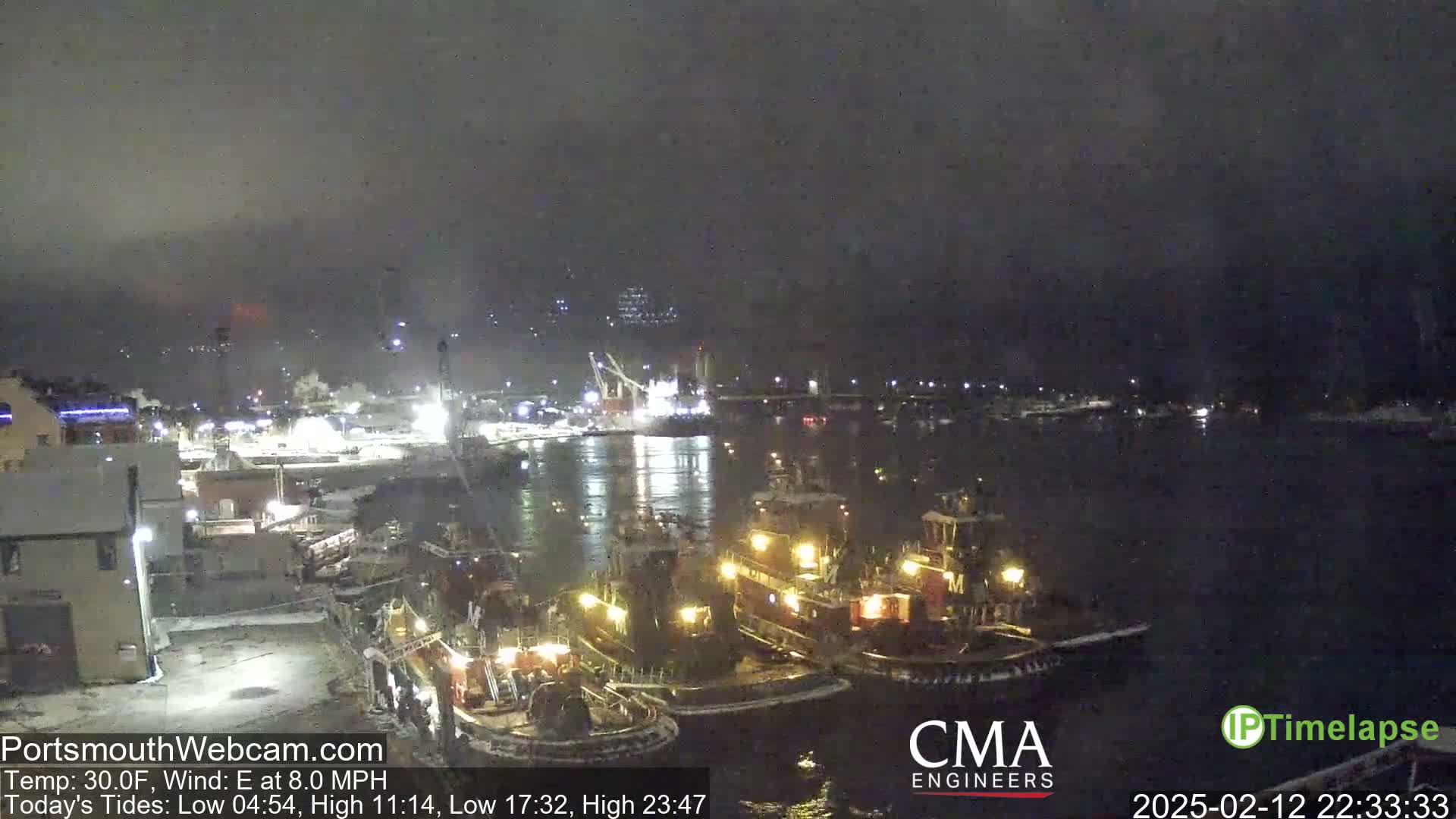 Several tugboats are docked at a harbor at night in snowy conditions.