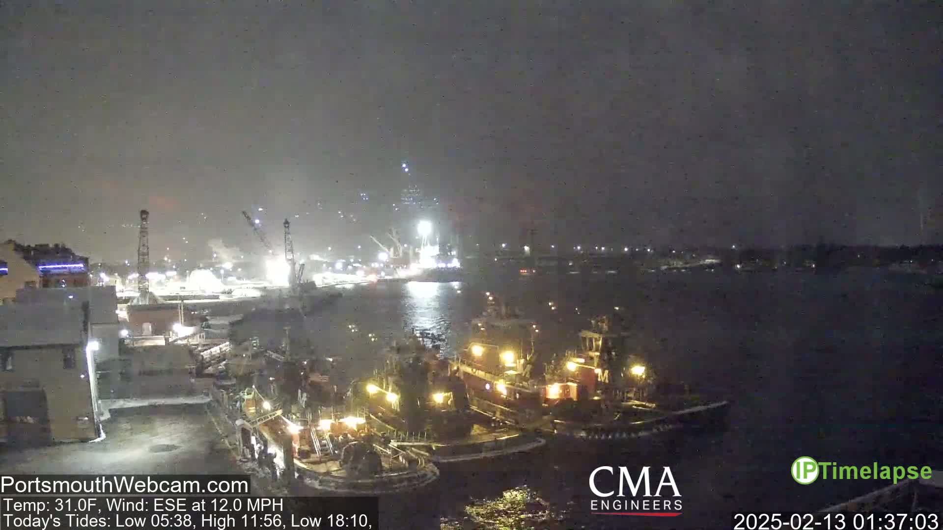 Several tugboats are moored near a dock at night in snowy conditions.